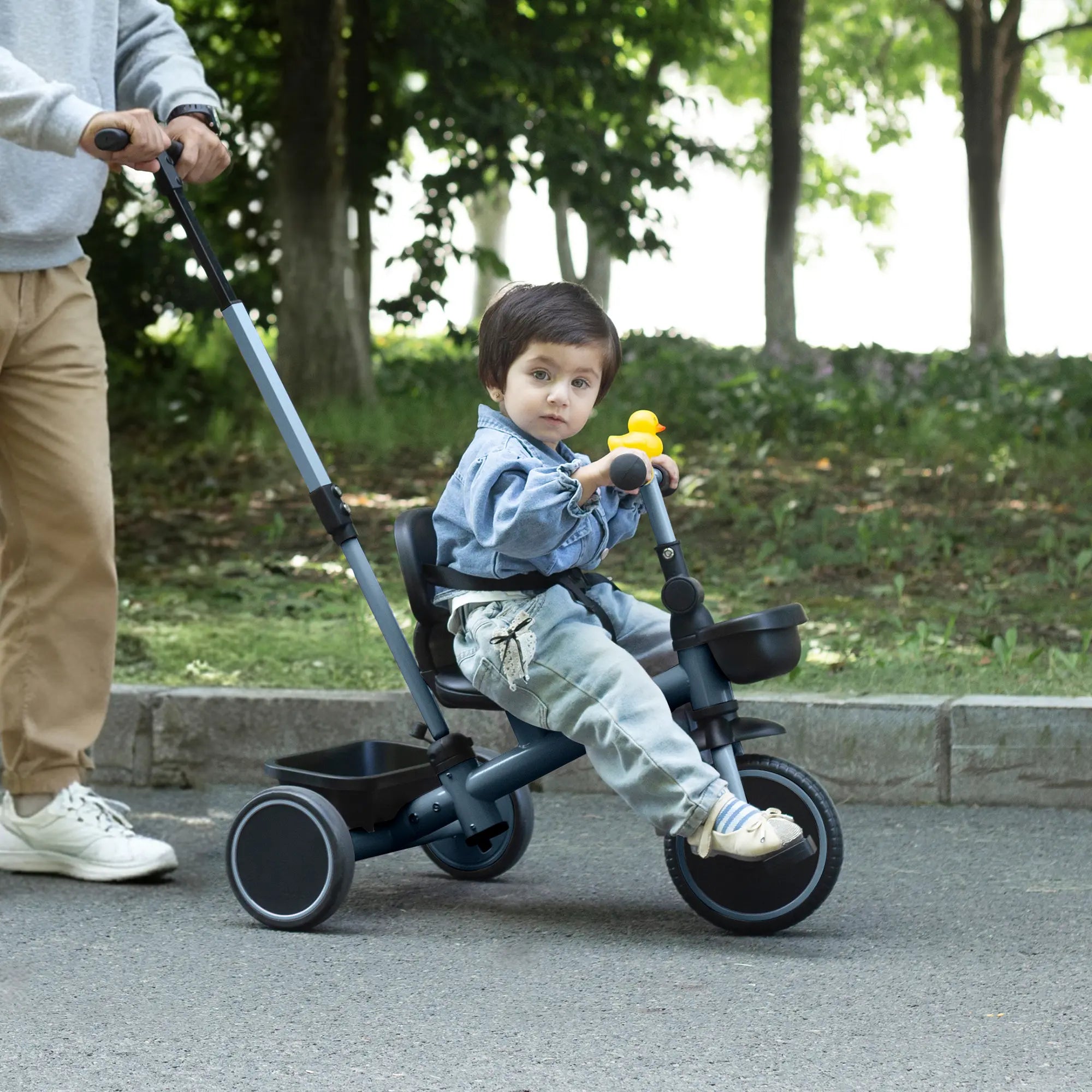 Child riding a trike with dad pushing it in a park setting