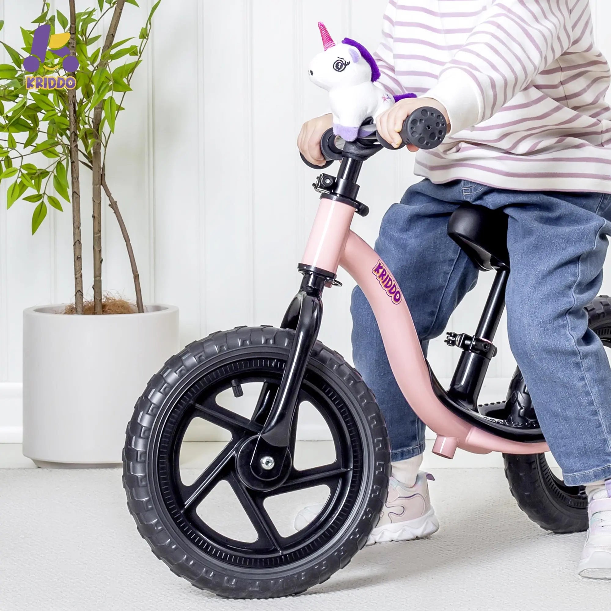 Child on a balance bike with a unicorn handlebar grip, indoors.