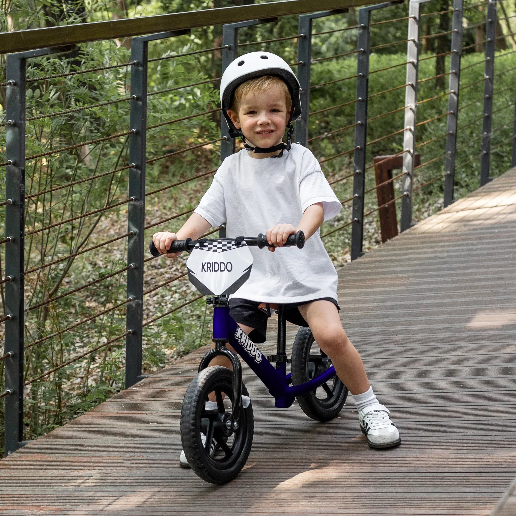 Kid riding KRIDDO 12 Inch blue balance bike on a wooden path