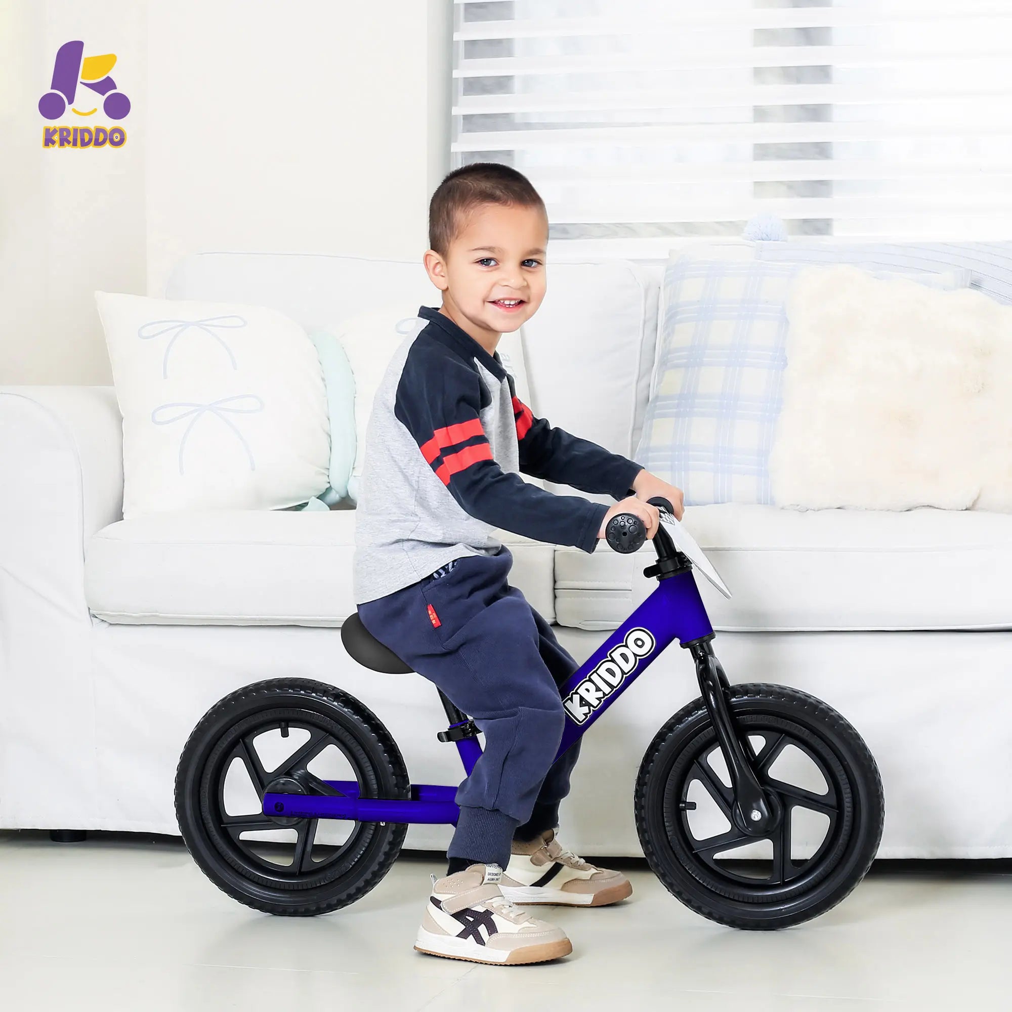 Child riding KRIDDO blue 12 inch balance bike in a living room