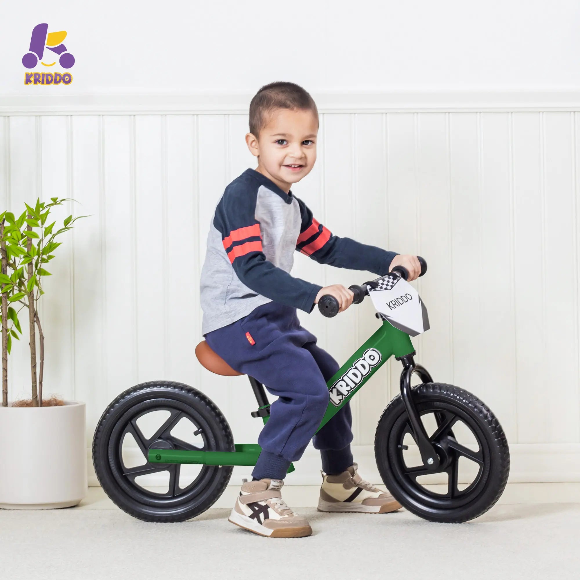 Boy riding KRIDDO Green 12 Inch balance bike in a living room.