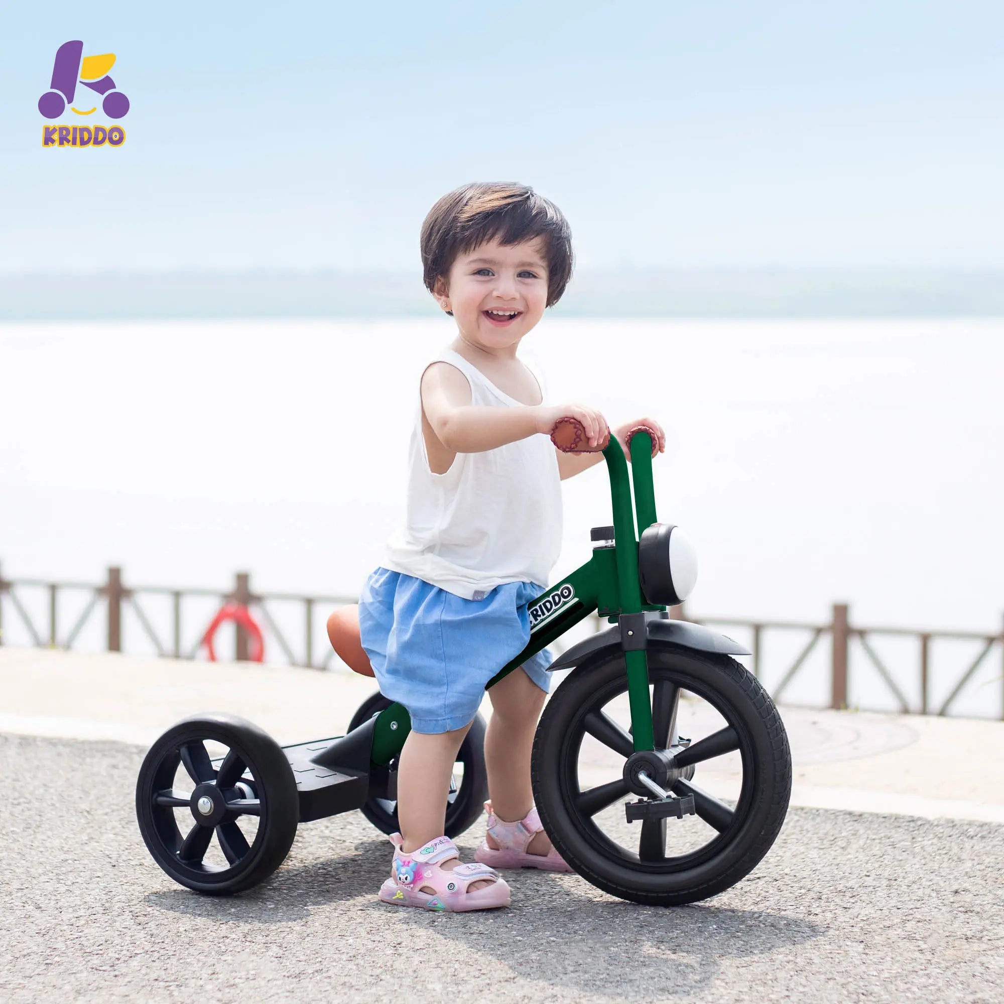 Girl riding KRIDDO green big wheel trike on a beach.