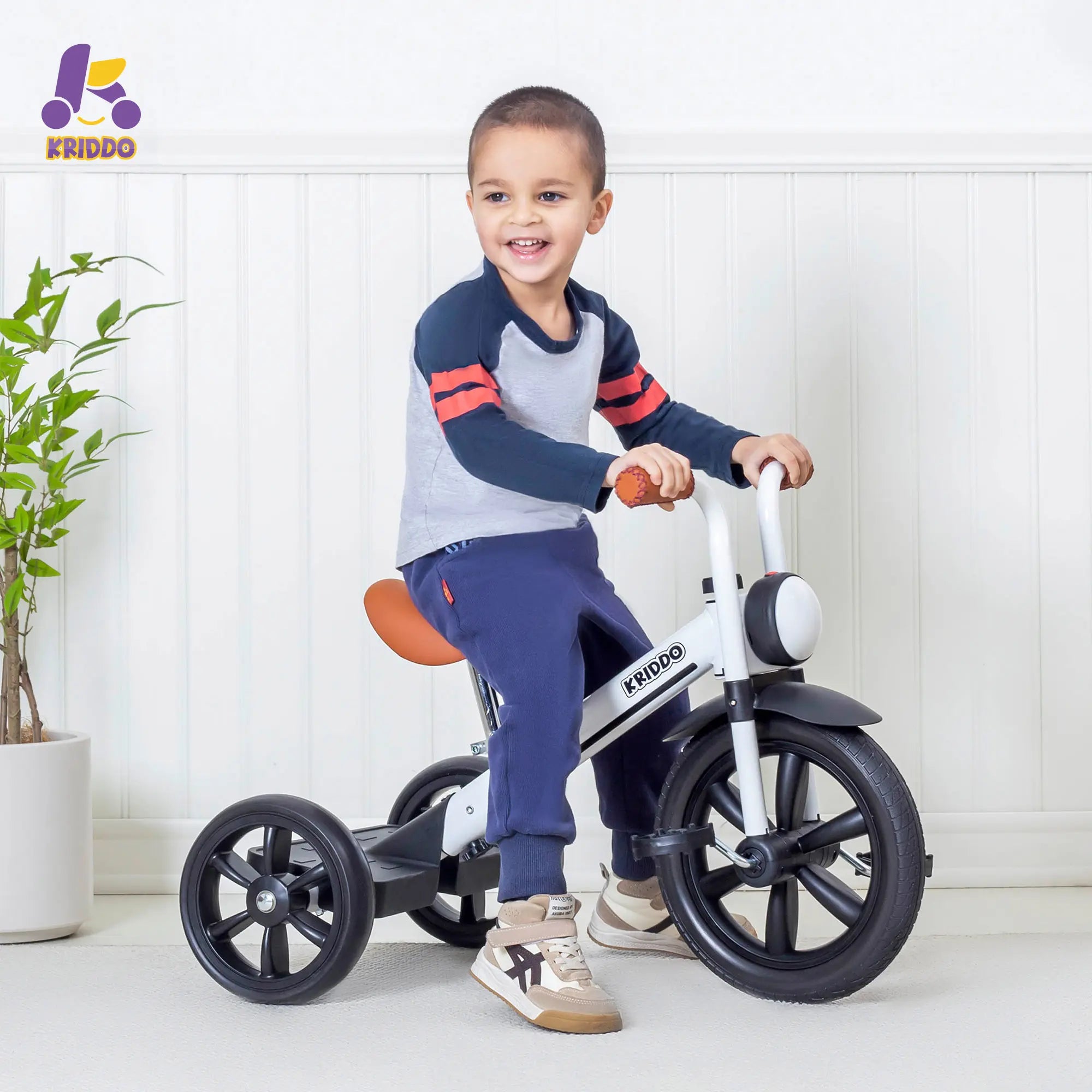 Toddler boy riding KRIDDO white trike in a bright room.