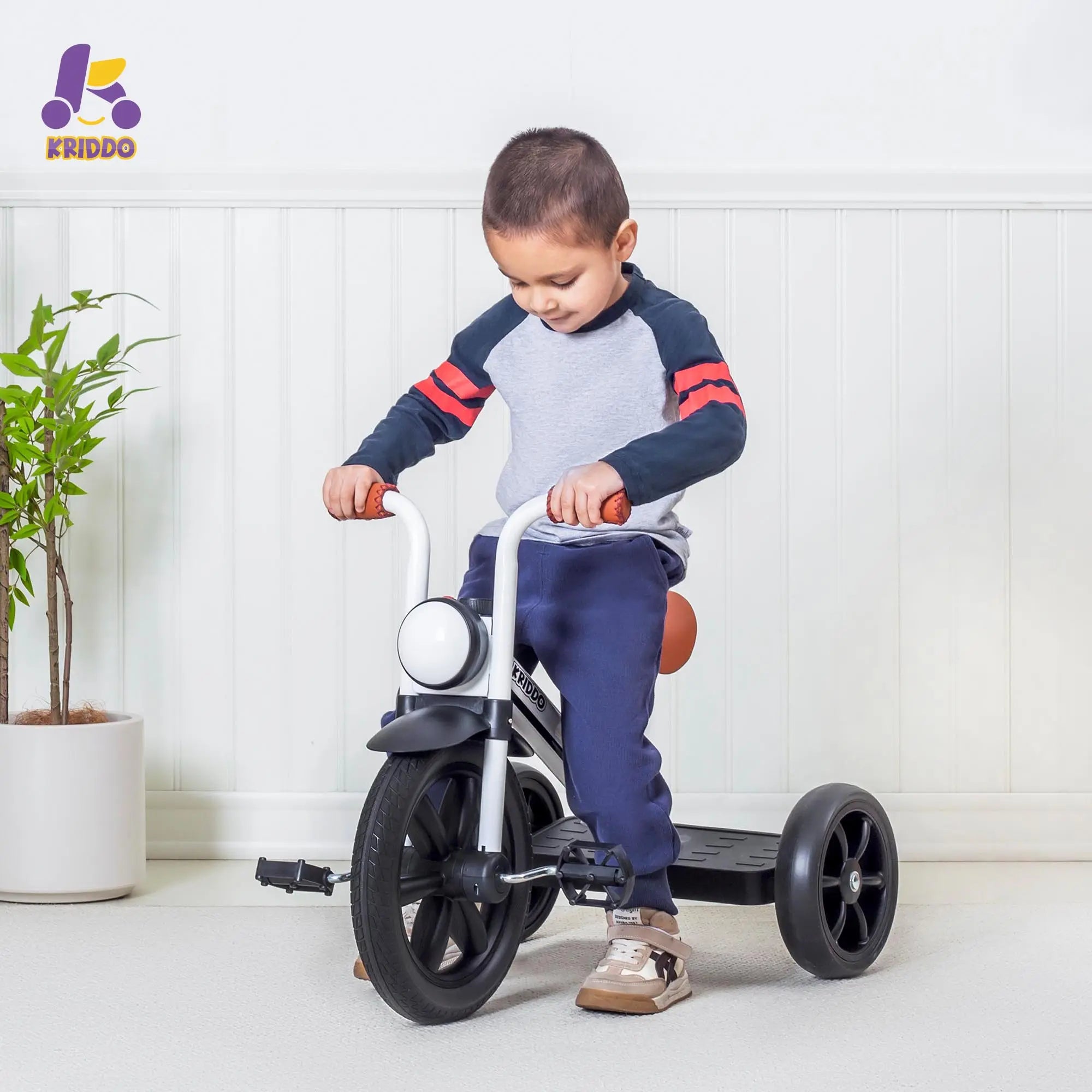 Child riding KRIDDO white tricycle with green plant