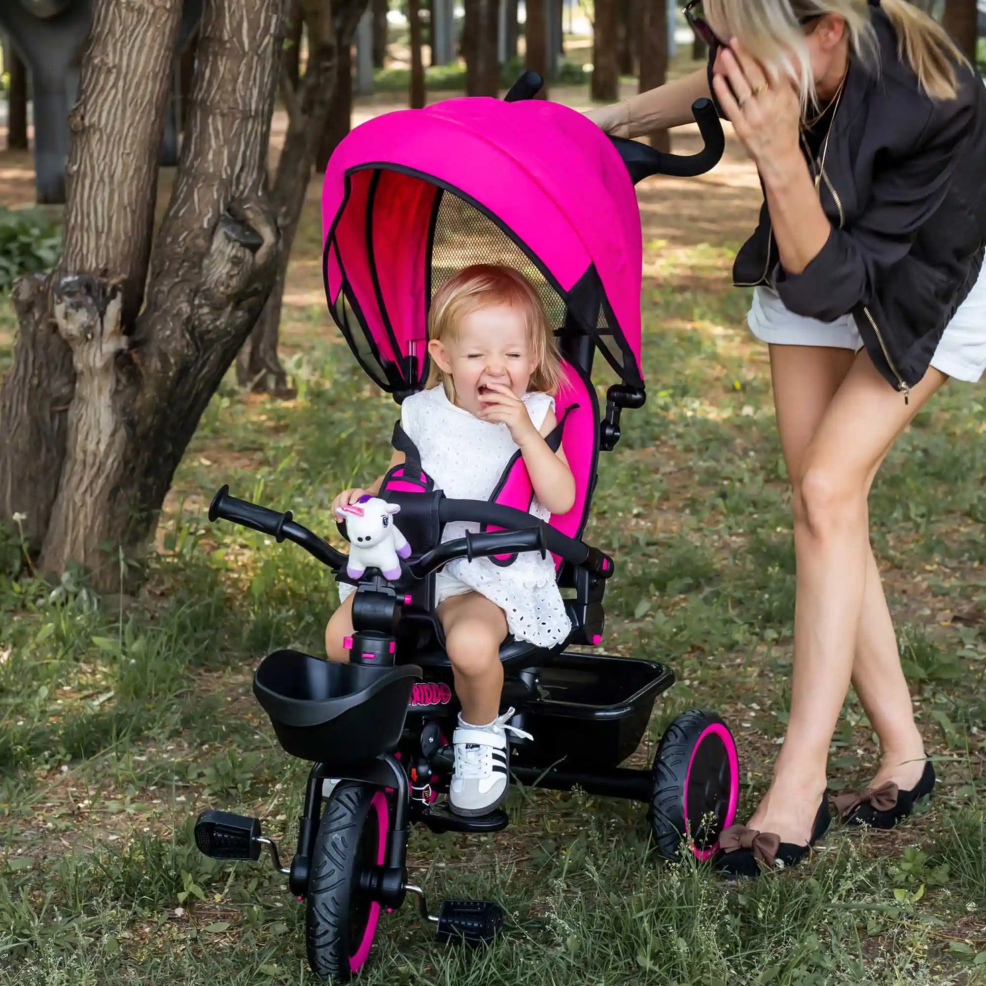 Child in KRIDDO Tricycle Stroller with mom standing nearby outdoors.