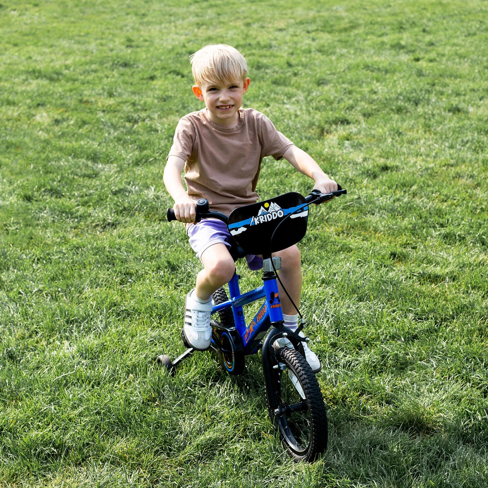 Toddler boy riding a KRIDDO 14 inch bike in a grassy field