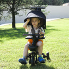 A toddler sits on KRIDDO foldable stroller trike outdoors on the grass