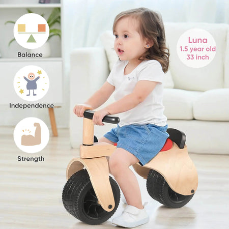 Child riding a baby wooden balance bike in a living room