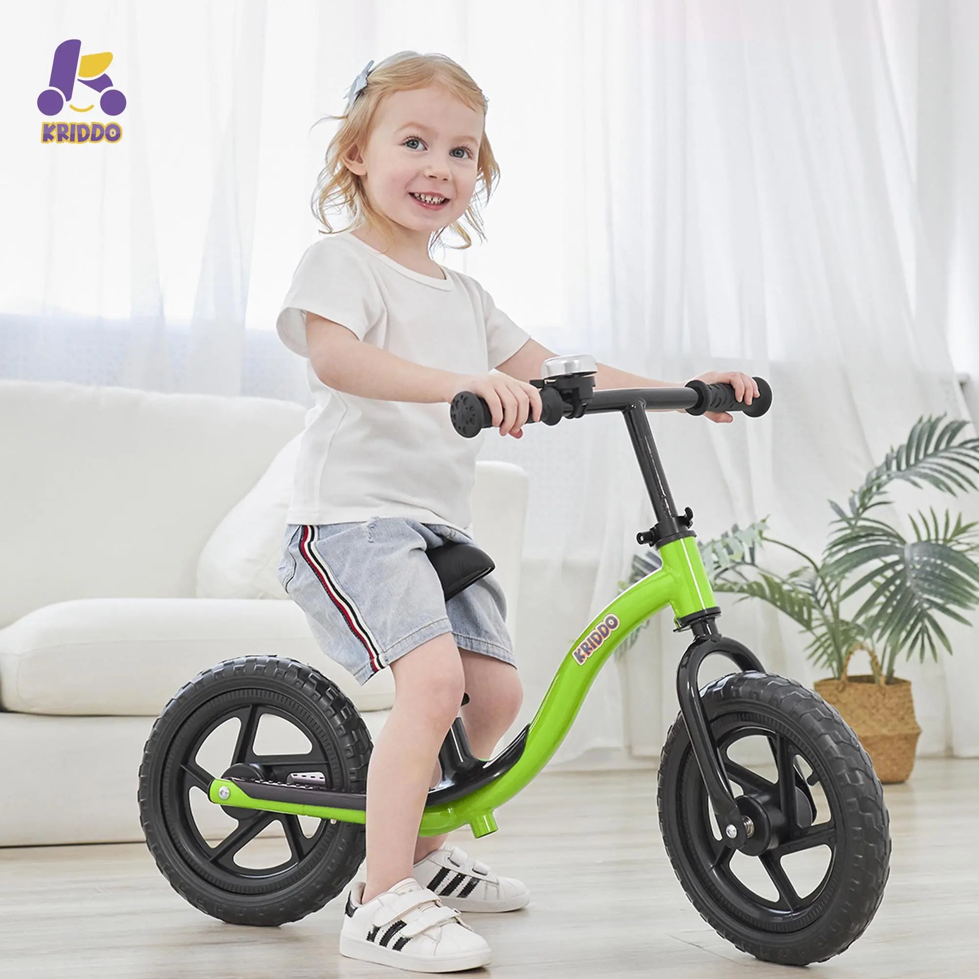Child riding KRIDDO green balance bike in a bright room