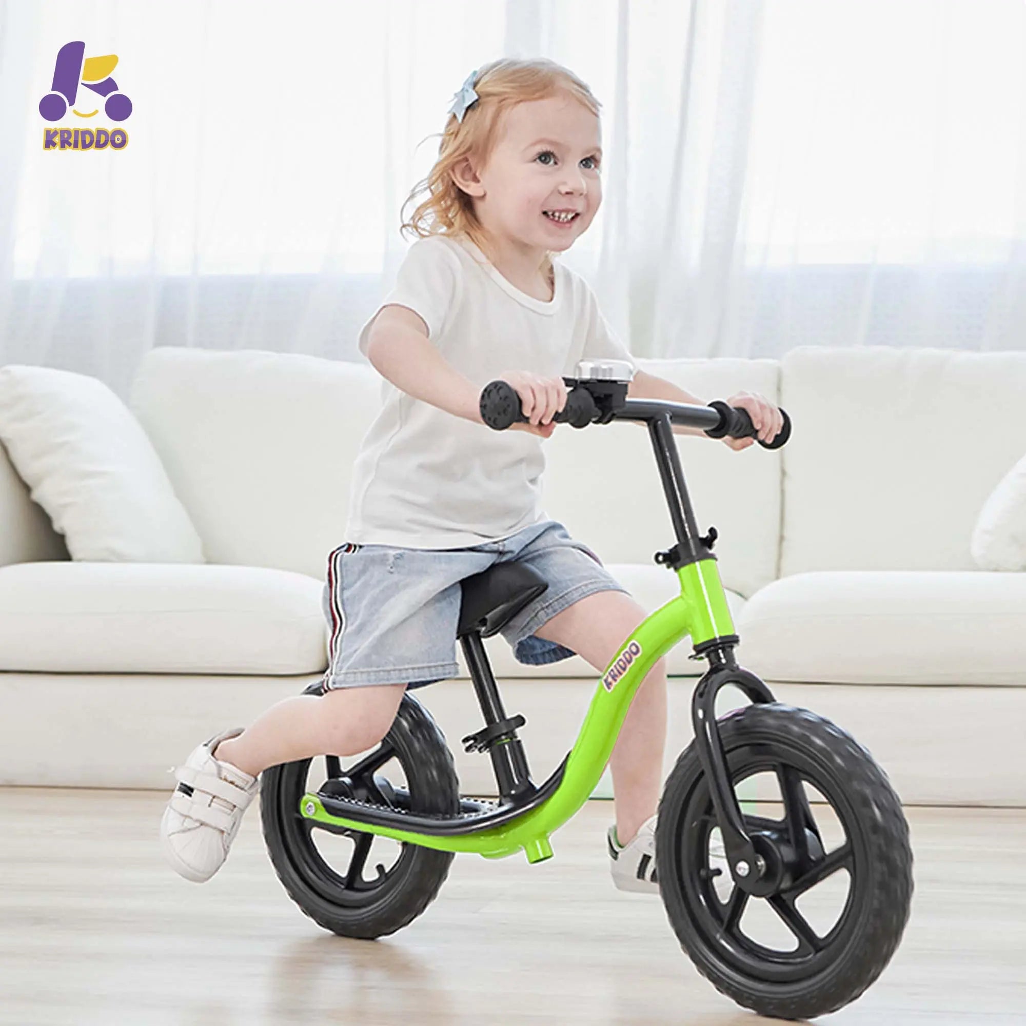 Toddler girl riding KRIDDO green balance bike in a living room