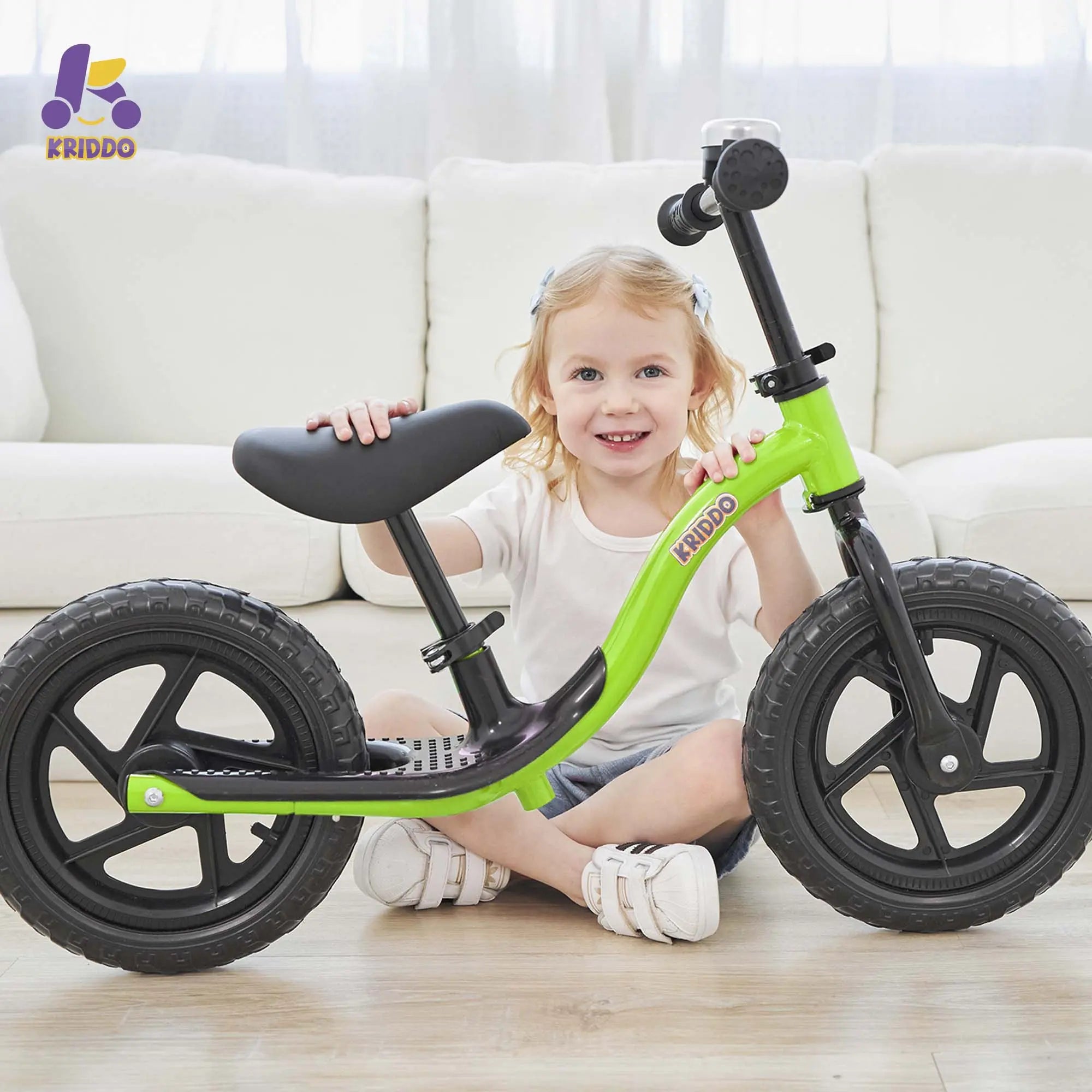 Child playing with KRIDDO green balance bike in a living room