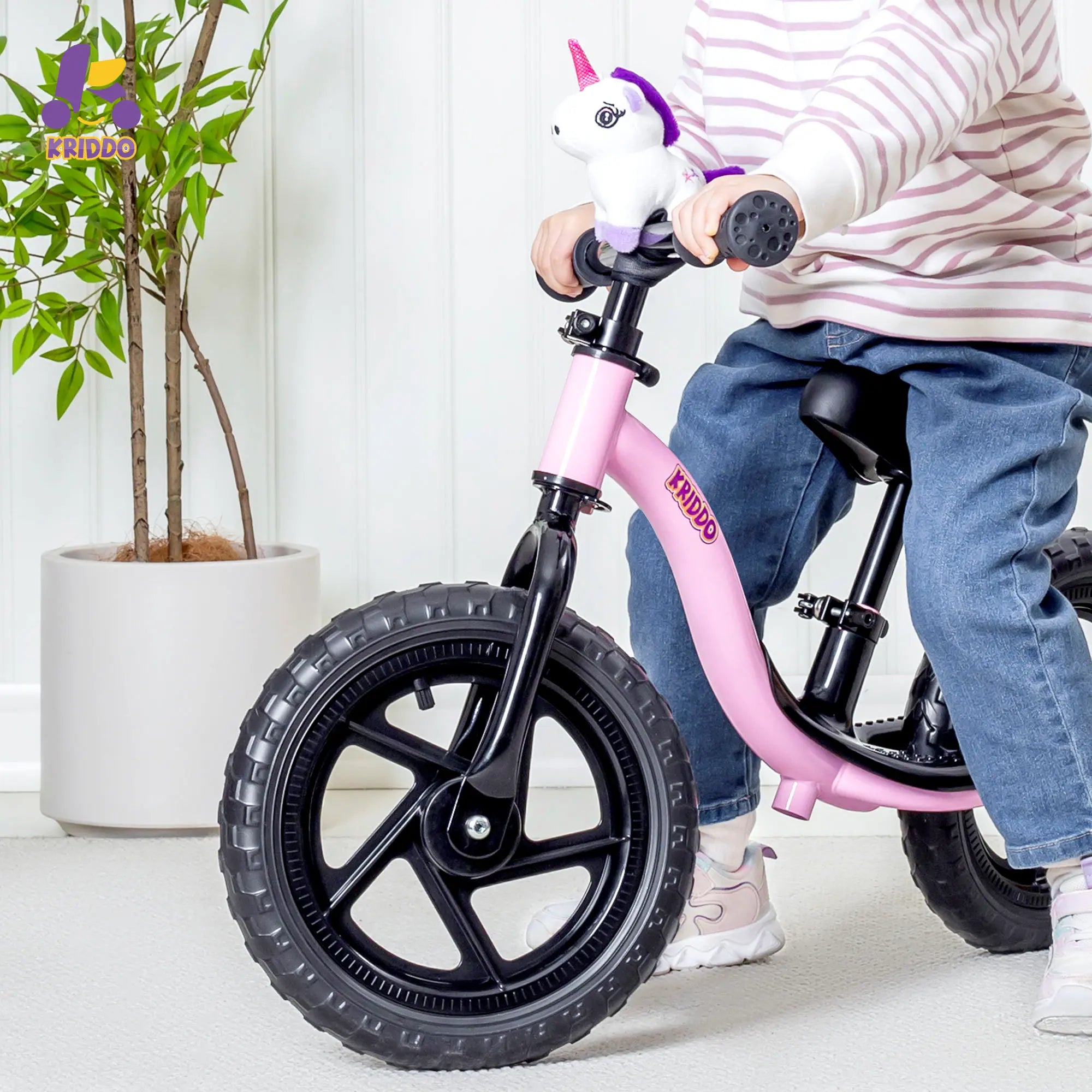 Child on a purple balance bike with a unicorn handlebar grip, indoors.