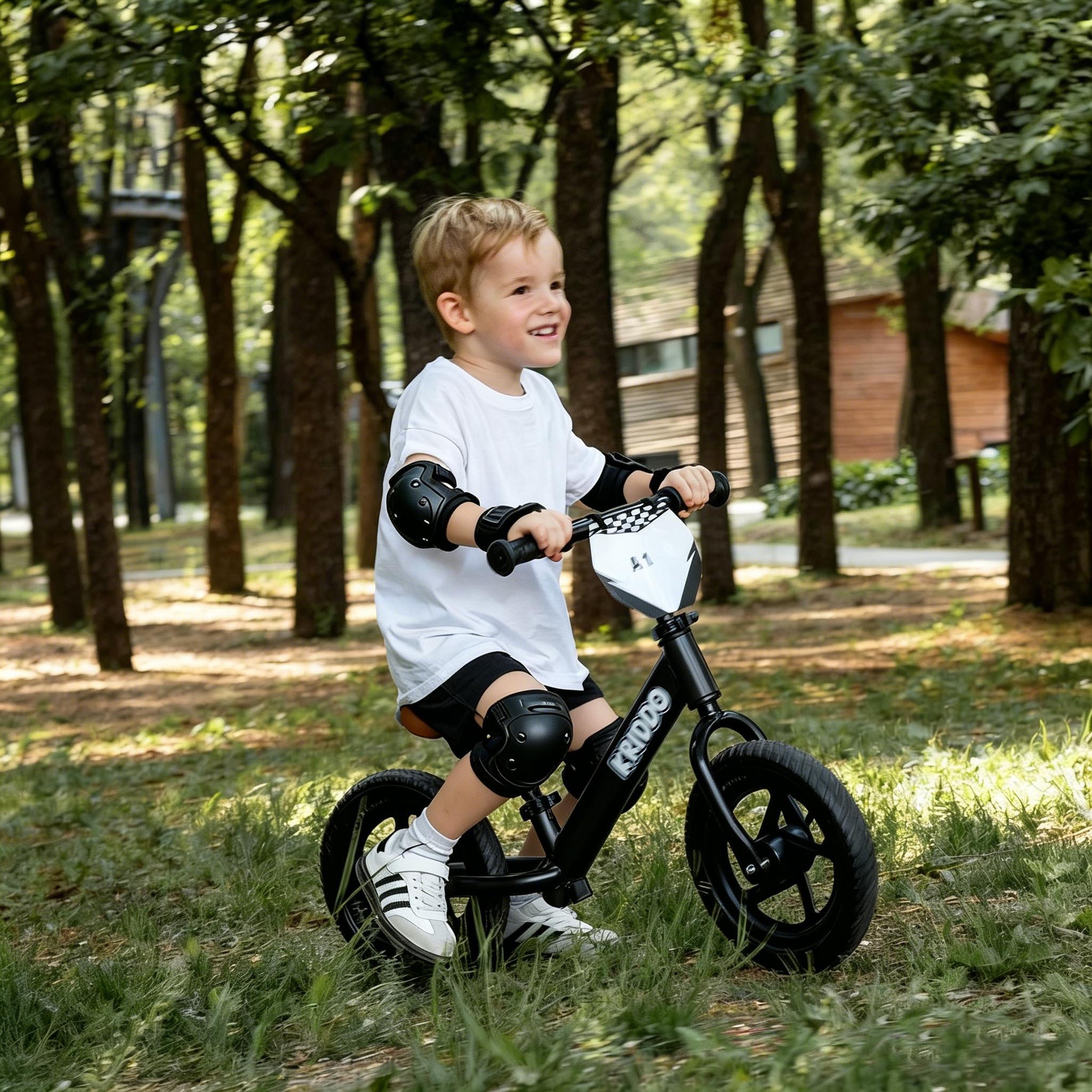 Toddler boy riding KRIDDO 12 inch balance bike on the grass with knee pads