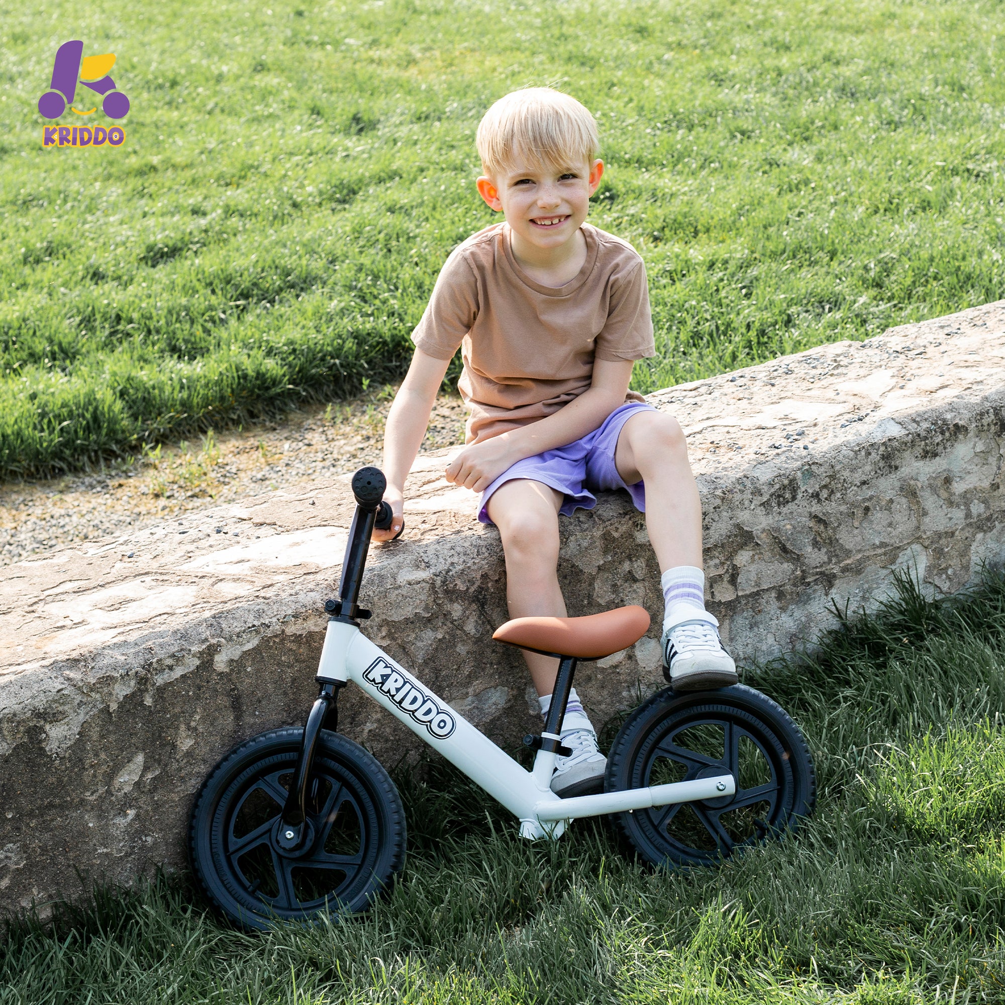 Child sitting on a stone ledge with a KRIDDO balance bike outdoors