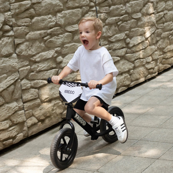 Kid riding KRIDDO 12 inch balance bike against a stone wall
