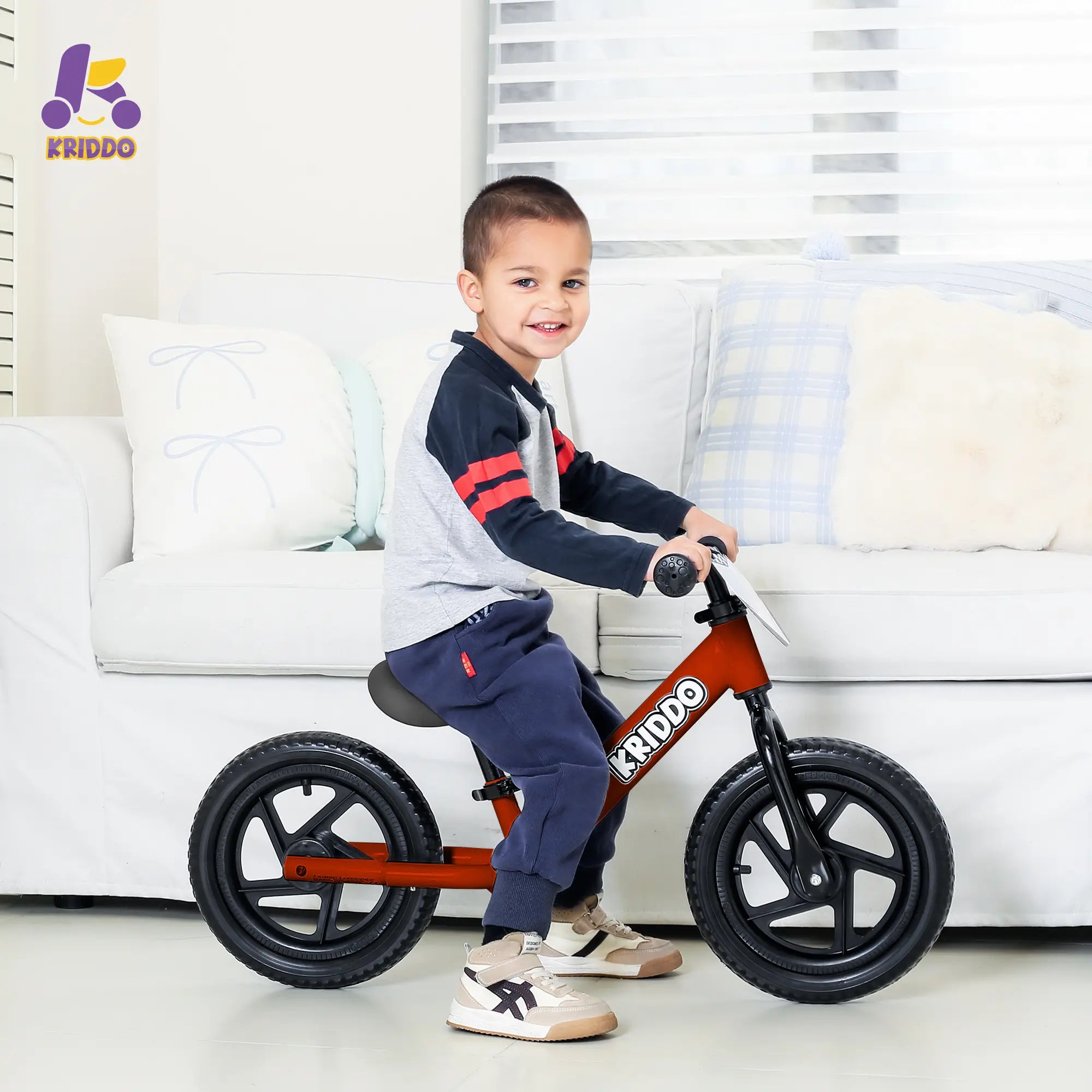 Boy riding KRIDDO red 12 Inch balance bike in a living room.