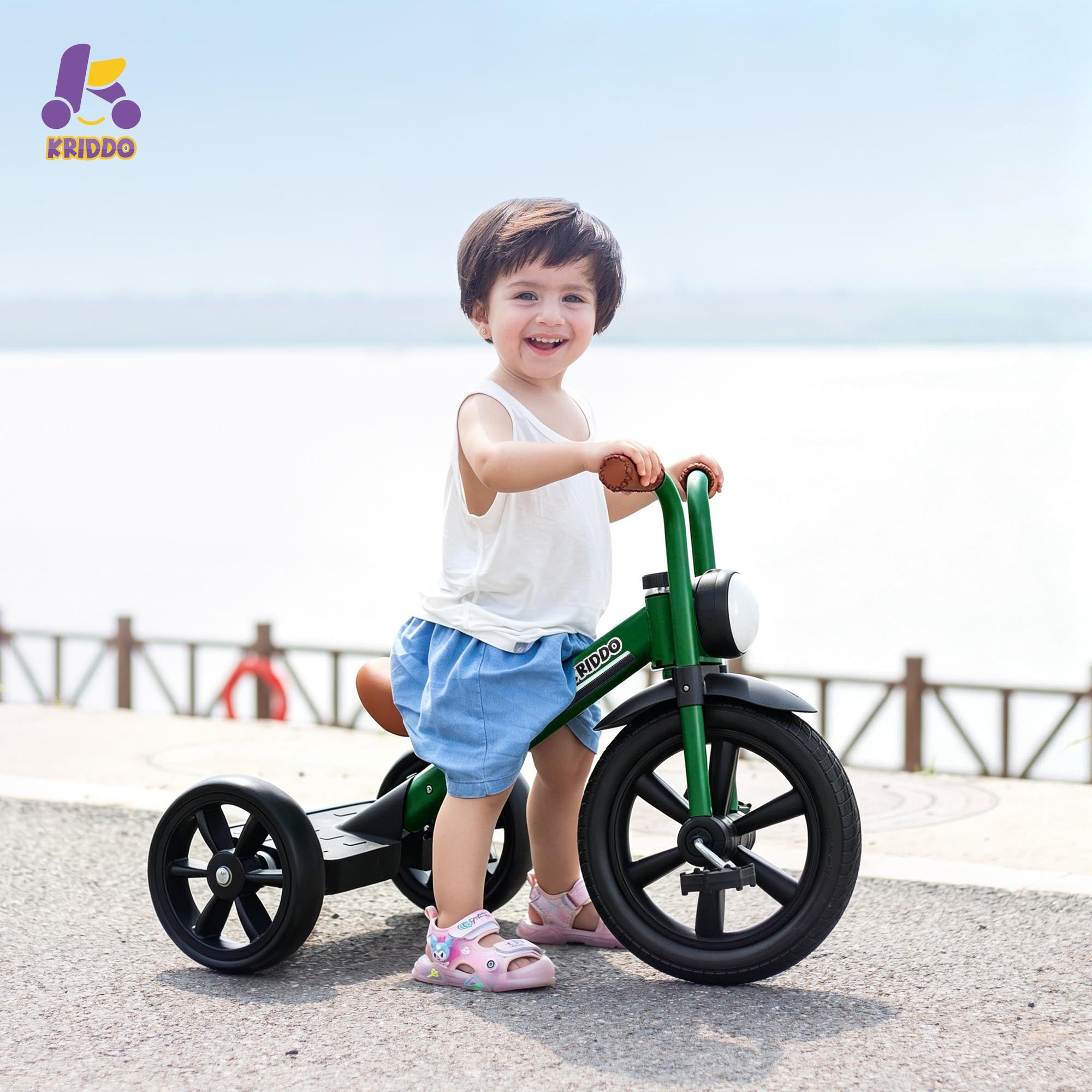 Child riding KRIDDO green tricycle on a beach