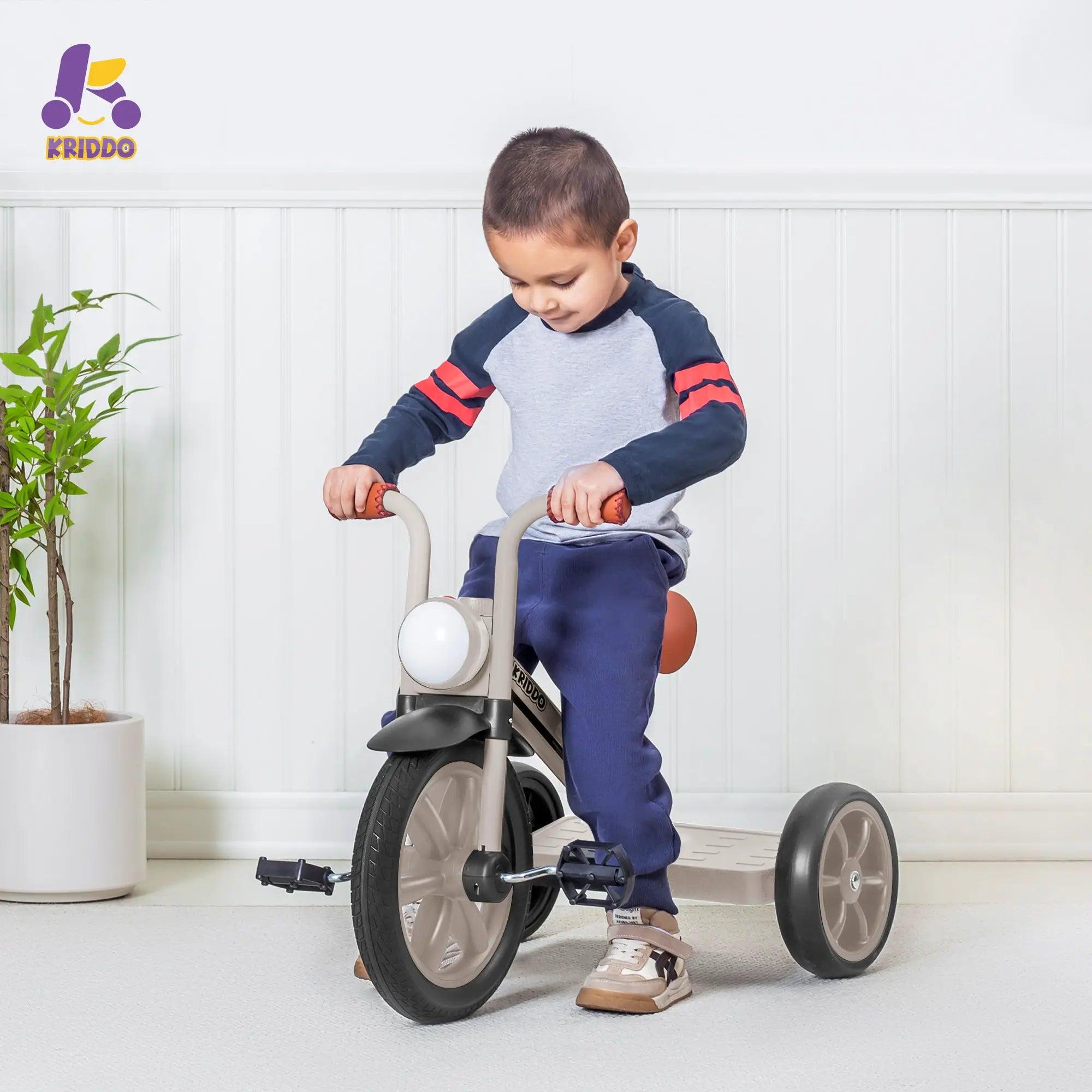 Child riding KRIDDO grey pedal tricycle indoors with a white wall and plant