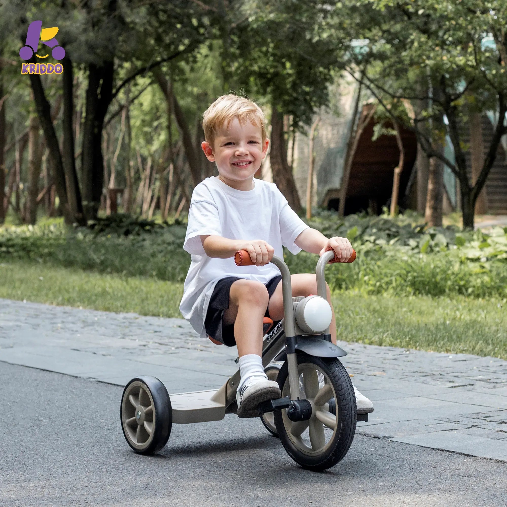 Little boy riding KRIDDO tricycle in a park with trees and grass
