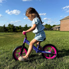 Girl riding KRIDDO light up balance bike in a grassy area with a clear sky
