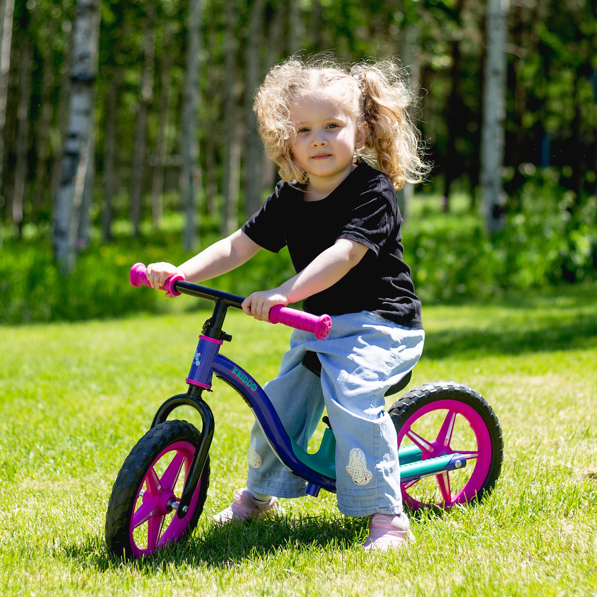 Child riding KRIDDO light upo balance bike in a park with green grass and trees.
