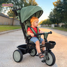A young child wearing a red shirt and denim shorts sits on a KRIDDO stroller trike with glowing wheels.