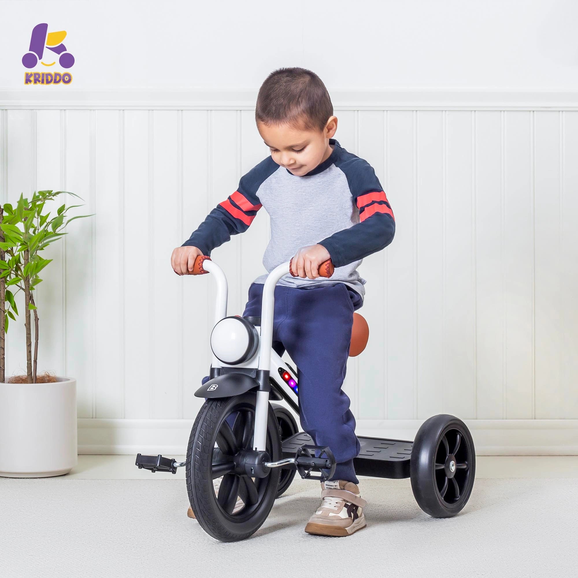 Child riding a light up tricycle indoors with a white wall and plant
